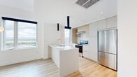 Located in Montréal's vibrant Old Port neighborhood, this modern 3-bedroom, 2-bathroom unit offers a thoughtfully designed layout with clean lines and a bright, contemporary aesthetic throughout. Light hardwood flooring flows consistently across every room, complemented by crisp white walls and recessed lighting that enhance the sense of openness.

The kitchen serves as a standout feature, centered around a sleek white island with an integrated sink. Flat-front cabinetry in white and natural wood tones lines the walls, paired with a subway tile backsplash, stainless steel appliances, and dramatic black pendant fixtures that add a bold contrast to the otherwise light palette. Large windows flood the space with natural light and frame impressive views of the Montréal skyline and waterfront.

Each of the three bedrooms is bright and well-proportioned, with large windows offering expansive city and river views. The hallways connect the rooms efficiently, maintaining a clean flow throughout. A dedicated closet provides additional storage convenience.

The two bathrooms are finished with large-format stone-toned floor tiles, warm wood-accented vanities, wide mirrors, and a full bathtub with a glass-paneled shower — combining practicality with a refined, spa-like quality. The overall design is cohesive, modern, and move-in ready.