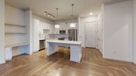 Located at 6000 Summit Pl in Alpharetta, Georgia, this single-floor residence combines modern design with functional living spaces. The open-concept kitchen and living area serves as the heart of the home, showcasing a striking herringbone-patterned hardwood floor that flows throughout the main living spaces. The kitchen is outfitted with crisp white shaker-style cabinetry, brushed nickel hardware, a geometric tile backsplash, and a full suite of stainless steel appliances including a gas range, built-in microwave, dishwasher, and French door refrigerator. A large central island with a white quartz countertop and pendant lighting above provides additional prep space and a natural gathering point. The living area features a tray ceiling with crown molding and French doors that invite natural light while offering outdoor access. Bedrooms are carpeted for comfort, with one featuring tall windows that fill the room with natural light. A generously sized walk-in closet with wire shelving provides ample storage. The bathroom is finished with large-format marble-look tile on both the floors and tub surround, complemented by a white vanity with brushed nickel hardware, offering a clean and polished aesthetic throughout.