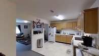 Located at 1000 Nicholas Brooks Ct in New Windsor, NY, this single-floor space offers a practical and functional layout designed for comfortable everyday living. The kitchen serves as a central feature of the home, equipped with ample honey-toned wood cabinetry providing generous storage both above and below the countertops. A full-size refrigerator, range, and microwave are included, alongside a dedicated sink area with a tiled backsplash. Light tile flooring runs throughout the kitchen, contributing to a clean and easy-to-maintain environment. Overhead fluorescent lighting ensures the space is well-lit. An open passageway connects the kitchen to an adjoining living area, which features carpet flooring and its own overhead lighting, creating a distinct but accessible transition between the two spaces. The living area offers a relaxed atmosphere with enough room for seating arrangements. The overall layout of the home is efficient and straightforward, making it well-suited for those seeking a manageable, single-level living environment in the New Windsor area.