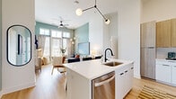 Located in Charlotte's vibrant Dilworth neighborhood, this three-bedroom, two-bathroom single-floor residence offers a thoughtfully designed open-concept layout with modern finishes throughout. Light hardwood flooring flows seamlessly across the entire space, creating a cohesive and airy feel.

The kitchen is a standout feature, showcasing a large white quartz waterfall island with an undermount sink and matte black faucet, two-tone cabinetry combining white lower cabinets with warm wood-tone uppers, and a full suite of stainless steel appliances including a range, microwave, and French door refrigerator. The kitchen opens directly into the living area, which is anchored by sage green accent walls, soaring ceilings, and floor-to-ceiling windows and doors that flood the space with natural light.

The primary bedroom is generously proportioned, featuring tall ceilings, large windows with exterior views, and direct access to a well-appointed en-suite bathroom with a walk-in glass shower, white floating vanity, and matte black fixtures. The second bathroom offers a clean, minimalist design with a tub-shower combo and equally refined finishes.

Two additional bedrooms provide flexible use, each benefiting from the home's bright, open atmosphere. A dedicated entrance, hallway, and closet complete the well-organized floor plan, making this a highly functional and stylish Charlotte residence.