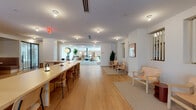 This expansive single-floor space is defined by a cohesive Scandinavian-inspired design language, blending natural materials, warm tones, and carefully curated furnishings throughout its multiple interconnected zones. The entry is anchored by a polished terrazzo floor and a sleek dark reception desk, with copper-toned metal railings guiding visitors up a set of steps to the elevated main level finished in wide-plank white oak hardwood.

The layout flows seamlessly from one area to the next, beginning with a welcoming lounge zone featuring a built-in walnut bench, a patterned area rug, and curated wall art. Adjacent seating areas offer a mix of modular sofas, rattan chairs, and an oversized globe pendant light, complemented by tall indoor plants that add organic warmth. Sheer floor-to-ceiling curtains diffuse natural light across these gathering areas.

A long communal work table with slender task lamps provides a dedicated workspace, while a dining nook with wood banquette seating and pendant lights serves as a more intimate setting. A distinctive curved curtain partition creates a semi-private area within the open floor plan. Throughout, terrazzo walls, slatted wood accents, and carefully placed artwork reinforce the space's refined yet approachable character.