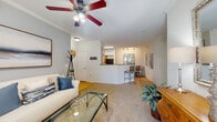 This single-floor residence offers a thoughtfully designed open-concept layout that seamlessly connects the living, dining, and kitchen areas. The living room is warm and inviting, featuring plush carpeting, crown molding, a ceiling fan with light fixture, and large French doors that invite generous natural light and provide access to the outdoors. Soft blue-grey accent walls and framed artwork contribute to the space's calm, welcoming ambiance.

The kitchen is outfitted with warm honey-toned cabinetry, granite-style countertops, and black appliances including a range, microwave, and dishwasher. Light hardwood-style flooring runs through the kitchen and dining areas, adding brightness and continuity. A peninsula counter with bar seating connects the kitchen to the dining and living spaces, making it well-suited for entertaining. Track lighting above the dining area provides focused illumination.

The bedrooms are carpeted and finished with crown molding and ceiling fans. Each room features ample natural light from windows with blinds, and closets with built-in shelving for storage. The primary bedroom is generously proportioned with room for full bedroom furnishings.

The bathroom features a long vanity with dark granite-style countertops, warm wood cabinetry, a single undermount sink, and large-format tile flooring. A separate water closet and shower area provide added privacy and functionality throughout this well-designed home.