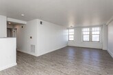 This single-floor unit presents a clean, functional layout with a clear separation between living areas and private rooms. The open living and dining area is finished with light-toned wood-style flooring that extends throughout the main living spaces, complemented by crisp white walls and smooth ceilings. Multiple large windows allow natural light to fill the space while framing urban views of the surrounding cityscape.

A peninsula-style kitchen sits adjacent to the main living area and is equipped with white shaker cabinetry, grey laminate countertops, a double stainless steel sink, a black electric range with overhead ventilation, a dishwasher, and a black refrigerator. The layout provides ample counter space and storage.

A hallway connects the living area to the private rooms, which feature neutral-toned carpet and windows offering additional natural light and outdoor views. One bedroom benefits from dual windows on adjoining walls, enhancing the sense of openness. The bathroom includes a white vanity with drawer storage, a large wall mirror with overhead lighting, and a full tub and shower combination. A built-in closet and recessed lighting add practical functionality throughout the unit.
