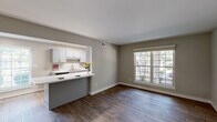 Located at 910 Shellbrook Ct in Raleigh, NC, this one-bedroom, one-bathroom residence offers a well-organized single-floor layout with a thoughtful blend of modern finishes and practical design. The open-concept living and dining area is anchored by rich, dark hardwood-style flooring and neutral gray walls, with a large multi-pane window that draws in generous natural light and frames views of the surrounding greenery. The kitchen is a standout feature, designed as a galley-style space with gray shaker cabinetry, marble-style countertops, a subway tile backsplash, skylights, and black stainless steel appliances including a refrigerator, range, and microwave. A pass-through counter connects the kitchen to the dining and living area, enhancing the open feel. The bedroom is a comfortable, well-proportioned room finished with plush carpeting, a ceiling fan, a window with outdoor views, and a spacious reach-in closet with double doors. The bathroom features a white shaker-style vanity with an undermount sink, a large mirror with overhead lighting, and hardwood-style flooring. Additional spaces include a utility room, hallway, and two closets, providing ample storage throughout.