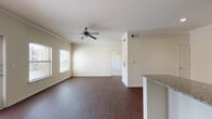 This single-floor residence offers a thoughtfully designed open-concept layout that seamlessly connects the living, dining, and kitchen areas. Rich, dark hardwood-style flooring flows throughout the main living spaces, complemented by neutral-toned walls and crown molding that lend a clean, polished aesthetic. Ceiling fans are installed in the living area and bedrooms, ensuring comfort throughout. Natural light enters through multiple windows fitted with blinds.

The kitchen is a standout feature, showcasing dark espresso cabinetry, granite countertops, a tile backsplash, and a full suite of stainless steel appliances including a refrigerator, range, microwave, and dishwasher. A breakfast bar provides additional counter space and connects the kitchen to the open living area.

The bedrooms are carpeted for comfort and feature ceiling fans and windows that bring in natural light. At least one bedroom includes a spacious walk-in closet with built-in shelving and hanging rods, offering generous storage.

The bathroom is well-finished with tile flooring, a tiled tub-and-shower combination, rich wood cabinetry, granite countertops, and a large vanity mirror with overhead lighting. Overall, the space presents a cohesive, modern interior with quality finishes throughout.