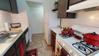 This single-story residence offers a practical and functional layout with well-defined living spaces. The galley-style kitchen is efficiently designed, featuring dark wood cabinetry on both upper and lower sections, white countertops, and a full suite of appliances including a gas range, dishwasher, and full-size refrigerator. A stainless steel sink sits beneath under-cabinet lighting, and stone-patterned tile flooring runs throughout the kitchen, extending toward a utility entry door at the far end. Open shelving above the refrigerator provides additional storage space.

The bedroom areas are carpeted in a neutral tone and feature built-in closets with shelving and hanging rods, offering ample storage. The rooms are bright with clean white walls, and structural beam detailing adds a subtle architectural element to the ceilings.

The full bathroom includes a tiled tub-and-shower combination, a small window for natural light and ventilation, white mosaic tile flooring, and standard fixtures in a clean, functional layout.

The living area is generously sized with wall-to-wall carpeting, open sightlines, and access to a walk-in closet or storage area, contributing to a comfortable and livable atmosphere throughout the space.