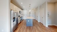 Located at 1100 Hampton Rivers Rd in Charleston, SC, this single-floor residence offers a well-designed open-concept layout that seamlessly connects the kitchen, dining, and living areas. Rich hardwood-style flooring runs throughout the main living spaces, complemented by neutral tones and abundant natural light streaming through multiple windows.

The kitchen is a standout feature, boasting crisp white shaker cabinetry with matte black hardware, a full suite of stainless steel appliances including a refrigerator with ice maker, electric range, built-in microwave, and dishwasher. A large center island with a light quartz countertop and a distinctive blue-gray base provides generous prep space and serves as a natural gathering point. Pendant lighting above the island adds a stylish finishing touch.

The spacious living area benefits from a ceiling fan, large windows framing views of the surrounding neighborhood, and sun-drenched hardwood floors. Bedrooms are carpeted for comfort and include ceiling fans and windows that bring in natural light. The bathroom features wood-look vinyl flooring, a tub-shower combination, a vanity with white cabinetry, and direct access to a walk-in closet equipped with built-in shelving and hanging rods. The overall design balances modern aesthetics with functional everyday living.