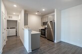 Located at 1200 Felix Way in Westampton, NJ, this single-floor 2-bedroom, 1-bathroom residence offers a clean, modern aesthetic with thoughtfully selected finishes throughout. The open-concept kitchen and living area serves as the heart of the home, featuring a peninsula with a built-in sink, crisp white countertops, gray shaker-style cabinetry, stainless steel appliances including a gas range and microwave, and warm wood-look flooring. The living area extends naturally from the kitchen and is bathed in natural light through sliding glass doors that open to an outdoor view. Both bedrooms are carpeted for comfort and maintain a bright, neutral palette. The primary bedroom offers generous proportions and includes a spacious walk-in closet with wire shelving and hanging rods for ample storage. The second bedroom features a large window that fills the room with natural light. The full bathroom is finished with elegant marble-look tile flooring, a gray vanity with sleek hardware, a large mirror with overhead lighting, and a full tub-shower combination. An in-unit washer and dryer area is also present, adding everyday convenience. Throughout, recessed lighting, crisp white walls, and clean trim work contribute to a cohesive and move-in-ready living environment.