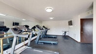 Located at 281 Country Village Dr in Smyrna, Tennessee, this fitness center is a well-equipped, single-floor facility divided into two dedicated exercise rooms. The space features durable speckled rubber flooring throughout, providing a practical and resilient surface suited for high-traffic workout use.

The first exercise room is outfitted with multiple treadmills, including Schwinn and other branded models, along with a stationary bike. Large wall-mounted mirrors line one side of the room, amplifying the sense of space and allowing users to monitor their form. A wall-mounted flat-screen TV is positioned for easy viewing during workouts. The room benefits from a glass entry door that allows natural light to filter in and offers views of the surrounding outdoor area.

The second exercise room features a multi-function cable strength training machine, an elliptical trainer, and additional cardio equipment. A water fountain station is conveniently installed along one wall, and a wall-mounted TV provides entertainment. A window offers a view to the exterior, bringing in natural light.

Both rooms are finished with neutral white walls, dark wood-toned baseboards and door trim, and flush-mount ceiling lights. The layout and equipment selection make this fitness center a comprehensive resource for both cardio and strength training needs.