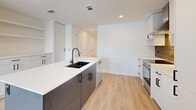 Located at 1330 S Fair St in Arlington, VA, this thoughtfully designed one-bedroom, one-bathroom residence offers a clean, contemporary aesthetic throughout. Light wood-look flooring flows seamlessly across the open-concept living area, connecting the living room, dining space, and kitchen into a cohesive and functional layout. The kitchen is a standout feature, showcasing flat-front white cabinetry with matte black hardware, a warm wood-toned backsplash, stainless steel range with a sleek hood vent, and a large center island with a white quartz countertop, undermount sink, and dark cabinetry base. Natural light pours in through floor-to-ceiling sliding glass doors that open to a private balcony, offering open views of the Arlington skyline. The bedroom is a bright, comfortable retreat with dual windows framing urban views and includes a built-in Murphy bed cabinet. Two closets provide generous storage, including a walk-in closet outfitted with adjustable shelving and hanging rods. The bathroom features tile flooring, a sleek dark-toned vanity with integrated sink, and direct access to the walk-in closet. In-unit laundry adds everyday convenience. Clean white walls and recessed lighting throughout contribute to a bright, modern ambiance.