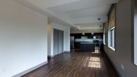 Located at 8 E Long St in the heart of Columbus, Ohio, this single-floor unit offers a thoughtfully designed open-concept layout that seamlessly connects the living area and kitchen. The kitchen is a standout feature, showcasing rich dark espresso cabinetry that extends to the ceiling, providing ample storage space. Granite countertops run throughout, including a central island that doubles as a breakfast bar, while stainless steel appliances — including a French door refrigerator, electric range, microwave, and dishwasher — complete the sleek, modern aesthetic. A decorative gold pendant light adds a warm, refined touch above the island. The open living area is bathed in natural light streaming through large windows, highlighting the rich, dark hardwood-style flooring that spans the entire space. Tray ceiling details add architectural interest and depth to the layout. A set of louvered closet doors provides practical storage without compromising the clean lines of the interior. The overall ambiance is modern and polished, with a cohesive dark-and-light contrast that gives the space a sophisticated urban feel, ideally situated in downtown Columbus.