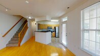 Located at 1115 Elmcroft Blvd in Rockville, Maryland, this three-story townhouse-style unit offers a thoughtfully organized layout across multiple levels. The entry level features an attached garage with an automatic door, providing secure, direct-access parking and additional storage space.

The main living level showcases warm hardwood flooring throughout the open living area, where track lighting and a staircase with a wood-railed banister contribute to the space's inviting character. The kitchen is well-appointed with light wood cabinetry, dark granite countertops, stainless steel appliances including a gas range, built-in microwave, refrigerator, and dishwasher, and tile flooring. A peninsula counter separates the kitchen from the living area, enhancing the open-concept flow. A door with a transom window provides natural light near the entry.

The upper levels host the bedrooms and bathrooms. The primary bedroom stands out with soaring vaulted ceilings, a ceiling fan, and three windows offering views of surrounding greenery. A full en-suite bathroom features tile flooring, a wood-toned vanity, and a glass-enclosed shower. Additional bedrooms are carpeted and receive natural light through windows overlooking wooded scenery. A second full bathroom includes a tub-shower combo and matching wood vanity.