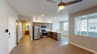 This single-floor residence offers a well-organized layout designed for comfortable, everyday living. The open-concept kitchen and living area forms the heart of the unit, where wood-look hard flooring connects the two spaces seamlessly. The kitchen is outfitted with dark-toned cabinetry, light quartz-style countertops, stainless steel appliances including a gas range, built-in microwave, and refrigerator, along with a peninsula featuring a deep undermount sink — an efficient and functional workspace. Recessed lighting illuminates the kitchen, while a ceiling fan serves the adjacent living area, which also benefits from natural light through window blinds. A keypad entry door is visible from the living space, adding a modern security feature. The bedrooms are carpeted and each includes a ceiling fan and windows with blinds providing outdoor views. One bedroom features sliding glass doors and direct access to a closet, while another includes a dedicated closet and direct access to an in-unit laundry room with a washer and dryer. The bathroom is cleanly appointed with a single-sink vanity, a large mirror, and a full soaking tub with shower. Throughout, the unit maintains a neutral color palette and consistent design language.