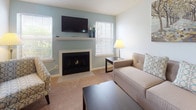 Located at 1212 Town Walk Dr in Hamden, Connecticut, this single-floor residence offers a thoughtfully designed layout with a cohesive, neutral color palette accented by soft blue-gray tones throughout. The open-concept living and dining area serves as the heart of the home, anchored by a classic fireplace framed by a white mantel and flanked by windows that allow natural light to fill the carpeted space. The living area provides a comfortable and inviting atmosphere ideal for both relaxing and entertaining. Adjacent to the living space, the dining area offers a defined space for meals and gatherings. The galley-style kitchen is efficiently arranged with white cabinetry, dark granite-style countertops, wood-look flooring, and full white appliances including a gas range and refrigerator. A tiled backsplash and ample upper and lower cabinet storage add to the kitchen's functionality. The bedroom is generously proportioned, featuring plush carpet, a large window with vertical blinds for light control, and a warm, restful ambiance. The full bathroom is clean and well-appointed, with a tub-shower combination featuring white tile surround, a white vanity, and wood-look flooring that ties the space together with the rest of the home.