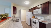 This single-floor unit at 2332 Asics Dr in Hilliard, Ohio offers a well-organized layout with distinct living, kitchen, bedroom, and bathroom areas. The kitchen is a functional galley-style space featuring dark espresso cabinetry, granite-look countertops, and white appliances including a refrigerator, electric range, and built-in microwave. A double-basin sink with a modern faucet completes the workspace, while a pass-through counter connects the kitchen to the main living area, promoting an open feel. The living area is finished with durable hardwood-style flooring and includes a sliding glass door that invites natural light and provides access to the outdoors. The bedrooms are carpeted for comfort, each featuring neutral-toned walls and windows with blinds that allow for natural light and privacy. Two bathrooms serve the unit; one includes a full tub-and-shower combination with a curved curtain rod, and both feature granite-top vanities with dark wood cabinetry and framed mirrors. Textured ceilings are consistent throughout, and the clean, neutral color palette gives the space a bright, cohesive appearance suited for a variety of interior styles.