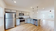 This well-appointed two-story home offers a thoughtfully designed layout with a bright, neutral color palette throughout. The main level features warm hardwood flooring that flows seamlessly from the open living area into the kitchen. The kitchen is a functional centerpiece, equipped with gray shaker-style cabinetry, granite countertops, a full suite of stainless steel appliances including a refrigerator, range, microwave, and dishwasher, as well as a peninsula with pendant lighting overhead. A convenient half bathroom on the main level includes hardwood flooring and matte black fixtures. The main level also provides access to additional utility areas and interior storage. A carpeted staircase with a clean white banister and warm wood handrail leads to the upper floor, where the bedrooms are located. The carpeted bedrooms are generously proportioned, with ceiling fans, natural light from windows with blinds, and a calm, neutral finish. The full bathroom on the upper level features a tub-shower combination, a white vanity with a clean countertop, hardwood flooring, and stylish mixed-metal hardware accents. Throughout the home, recessed lighting, panel-style interior doors, and crisp white walls create a fresh, move-in-ready atmosphere.