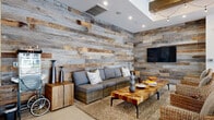 Located at 1100 E Bell Rd in Phoenix, AZ, this generously proportioned single-story clubhouse delivers a compelling rustic-modern aesthetic across a thoughtfully designed open-concept floor plan. Polished concrete floors run throughout the entire space, providing a clean, cohesive foundation that complements the warm, natural materials layered above.

The main lounge area is anchored by a classic brick fireplace and a richly textured reclaimed wood accent wall, with sculptural white ceiling fixtures adding an artistic overhead focal point. Natural light pours in through large windows, keeping the atmosphere bright and welcoming. Comfortable seating arrangements with wicker and upholstered chairs invite relaxed conversation and socializing.

Transitioning deeper into the space, exposed dark wood ceiling beams and strung Edison bulb lighting create a warm, industrial-chic ambiance over the central game area, which features a shuffleboard table and pool table. A second reclaimed wood accent wall—this one in a weathered grey-and-tan palette—defines the lounge nook, outfitted with a plush sectional sofa and wall-mounted TV.

A bar-height dining and lounge zone offers counter seating alongside high-top tables, adjacent to a kitchenette area. A sliding barn door on a black iron rail adds a stylish, functional divider near the entry. Large garage-style glass doors connect the interior to an outdoor patio, seamlessly blending indoor and outdoor living.