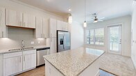 Located at 3030 Greenbusch Rd in Katy, TX, this thoughtfully designed one-bedroom, one-bathroom residence offers a comfortable and modern living experience across a single floor. The open-concept kitchen is a standout feature, showcasing granite countertop surfaces, a central island with pendant lighting overhead, light wood-toned cabinetry, a subway tile backsplash, and a full suite of stainless steel appliances including a refrigerator with ice maker, electric range, over-the-range microwave, and dishwasher. Wood-look flooring runs throughout the main living and kitchen areas, lending warmth and continuity to the space. The living room benefits from natural light streaming through large windows with views of greenery outside, and a ceiling fan adds comfort. The generously sized primary bedroom features plush carpet, large windows framing outdoor views, a private door to the exterior, and a ceiling fan. A built-in shelving nook connects the living area to the bedroom corridor, providing additional storage and display space. The bathroom is clean and modern, with granite-topped vanity cabinetry, a glass-enclosed tiled shower, and wood-look flooring. A walk-in closet with multi-level shelving and hanging rods completes the bedroom suite.