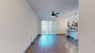 This single-story, one-bedroom, two-bathroom unit offers a thoughtfully organized layout across a compact but efficient floor plan. The open-concept living and kitchen area forms the heart of the space, where hardwood-style flooring flows throughout. The kitchen features stainless steel appliances, including a refrigerator, range, and microwave, complemented by a mix of warm wood-tone and light cabinetry, a tile backsplash, stone-look countertops, a central island, and globe pendant lighting overhead. The living area benefits from natural light streaming through a full sliding glass door fitted with vertical blinds, offering outdoor views and access. A ceiling fan with an integrated light fixture serves both the living room and the bedroom.

The bedroom is a comfortable size with carpeted flooring, a ceiling fan, and direct access to a dedicated closet equipped with a full-length shelf and hanging rod. Both bathrooms are finished in a modern style; one features a sleek floating vanity with a stone countertop, under-mount sink, and backlit LED mirror. A dedicated laundry room houses a full-size washer and dryer with an overhead wire shelf. A hallway connects the rooms efficiently, completing this well-appointed unit.