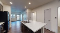 This single-floor space is designed with a clean, contemporary aesthetic that balances functionality and style. The kitchen serves as the heart of the unit, anchored by a central island topped with a white, textured countertop and equipped with a double stainless steel sink and a modern pull-down faucet. Dark espresso-toned cabinetry lines the walls, providing generous storage, while stainless steel appliances — including a refrigerator, electric range, and over-the-range microwave — complete the well-appointed cooking space. Rich hardwood-style flooring extends throughout the kitchen and living areas, adding warmth and visual continuity.

The open layout connects the kitchen seamlessly to the living area, which benefits from natural light through windows near the entry door. A full bathroom features a soaking tub with a shower surround, a toilet, and a dark-cabinetry vanity, with hardwood-style flooring tying the room together. The bedroom is carpeted for comfort and includes a window that brings in natural light and outdoor views. Recessed lighting throughout the unit ensures consistent, clean illumination across all spaces.