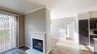This single-floor residence offers a well-organized layout that balances open living spaces with practical functionality. The living room serves as a central focal point, anchored by a classic white-mantled fireplace with a glass-front surround. Wood-look flooring runs throughout the main living areas, complemented by crown molding and neutral gray walls that lend a clean, contemporary feel. Large vertical blinds allow natural light to filter in while maintaining privacy, and views of greenery outside add a welcoming touch.

The kitchen is a standout feature, showcasing dark espresso cabinetry with modern hardware, a gray subway tile backsplash, light quartz countertops, and a full suite of stainless steel appliances including a refrigerator, range, microwave, and dishwasher. A center island provides additional workspace and storage, making the kitchen both stylish and highly functional.

The bedroom is carpeted for comfort, fitted with a ceiling fan, and receives ample natural light through a window with blinds. The bathroom includes a tiled shower-tub combination, vanity with mirror, and wood-look flooring. A dedicated laundry area with full-size washer and dryer connections and built-in shelving adds everyday convenience.