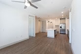 This single-floor unit presents a clean, modern aesthetic carried consistently throughout its layout. The kitchen serves as a functional centerpiece, featuring gray shaker-style cabinetry, white quartz countertops, a subway tile backsplash, and a full suite of stainless steel appliances including a French door refrigerator, electric range, over-the-range microwave, and dishwasher. A kitchen island with an integrated sink provides additional prep space and casual seating potential, while pendant lighting adds a contemporary touch overhead.

Wood-look luxury vinyl plank flooring runs throughout the main living areas, offering both durability and visual warmth. The open living space is bright and clean, with white walls and a straightforward layout that allows for flexible furniture arrangements. A doorway connects to a carpeted room, likely a bedroom, complete with a ceiling fan.

The unit includes two bathrooms. One features a tub-shower combo with white subway tile surround, a toilet, and wood-look flooring. The second, likely a primary bath, includes a walk-in glass-door shower with white tile, a single-sink vanity with a white countertop and gray cabinetry, and direct access to a built-in walk-in closet with multi-level shelving and hanging rods. Overall, the unit delivers a cohesive, functional, and well-finished living environment.