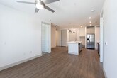 This single-floor unit presents a clean, modern aesthetic carried consistently throughout its layout. The kitchen serves as a functional centerpiece, featuring gray shaker-style cabinetry, white quartz countertops, a subway tile backsplash, and a full suite of stainless steel appliances including a French door refrigerator, electric range, over-the-range microwave, and dishwasher. A kitchen island with an integrated sink provides additional prep space and casual seating potential, while pendant lighting adds a contemporary touch overhead.

Wood-look luxury vinyl plank flooring runs throughout the main living areas, offering both durability and visual warmth. The open living space is bright and clean, with white walls and a straightforward layout that allows for flexible furniture arrangements. A doorway connects to a carpeted room, likely a bedroom, complete with a ceiling fan.

The unit includes two bathrooms. One features a tub-shower combo with white subway tile surround, a toilet, and wood-look flooring. The second, likely a primary bath, includes a walk-in glass-door shower with white tile, a single-sink vanity with a white countertop and gray cabinetry, and direct access to a built-in walk-in closet with multi-level shelving and hanging rods. Overall, the unit delivers a cohesive, functional, and well-finished living environment.