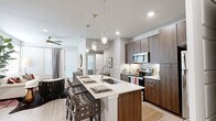 This thoughtfully designed single-floor residence offers a seamless blend of modern style and practical living across a well-utilized footprint. The open-concept kitchen and living area serves as the heart of the home, anchored by a large center island with a white quartz countertop, an integrated sink, and seating for multiple guests. Rich dark wood cabinetry, a decorative tile backsplash, and stainless steel appliances — including a range, microwave, and refrigerator — complete the kitchen. Stylish pendant lighting illuminates the island, while recessed lighting brightens the full space. Light wood-tone flooring flows throughout the main living areas, complementing the neutral gray walls and large windows that invite generous natural light into the living room. The bedroom features plush carpeting and a calm, restful atmosphere. The bathroom is elegantly appointed with a dual-sink vanity with wood cabinetry and white countertops, a frameless glass walk-in shower with large-format tile, and light wood flooring. A spacious walk-in closet with built-in shelving and hanging rods provides ample storage. Completing the unit is a dedicated in-unit laundry area with a full-size washer and dryer.