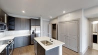 Located in Plano, this single-floor residence showcases a thoughtfully designed kitchen as its centerpiece. The kitchen features dark espresso-toned cabinetry that extends to the ceiling, providing generous storage capacity. A central island with a crisp white countertop and an undermount stainless steel sink serves as both a functional workspace and a casual gathering spot. The faucet is a sleek, modern pull-down style that complements the overall aesthetic. Stainless steel appliances, including a French door refrigerator with an in-door ice and water dispenser and a dishwasher, add a polished, contemporary feel. A white subway tile backsplash provides a clean contrast to the darker cabinetry. Recessed lighting illuminates the space efficiently, highlighting the warm wood-look plank flooring that runs throughout. A walk-in closet with visible shelving is accessible just off the kitchen area, offering practical storage solutions. Double doors with raised paneling lead to an additional storage or utility space. The neutral white walls and light-toned ceilings keep the space feeling open and bright.