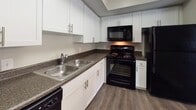 This single-story residence offers a well-organized layout with a variety of functional spaces. The living area serves as a central gathering point, featuring dark hardwood-style flooring, a classic white-mantled fireplace with tile surround, and a textured ceiling. Natural light filters in through a sliding glass door fitted with vertical blinds, which opens to an outdoor area, and an additional window enhances the brightness of the connected dining space, illuminated by a pendant light fixture.

The kitchen is efficiently designed with white shaker-style cabinetry, dark granite-look countertops, a double stainless steel sink, and a full suite of black appliances including a range, microwave, dishwasher, and refrigerator. The hardwood-style flooring continues seamlessly throughout this area.

The bedrooms are carpeted and feature neutral wall tones, ceiling fans with light fixtures, and ample closet access. One bedroom includes a walk-in closet and direct access to additional rooms. The bathroom is finished with white tile surrounds and includes a full soaking tub with shower. Textured ceilings are consistent throughout, contributing to a cohesive and practical interior aesthetic.