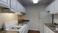 This two-floor space is designed with functionality and practicality in mind. The kitchen is a standout area, featuring crisp white upper and lower cabinetry that provides ample storage. Dark laminate countertops offer a contrasting accent against the white cabinetry, creating a classic and clean aesthetic. The kitchen is equipped with a white gas range and a full-size white refrigerator, making it well-suited for everyday cooking needs. An under-cabinet range hood is positioned above the stove, enhancing ventilation. The kitchen floor features rich, dark hardwood, adding warmth to the overall space. Overhead, a flush-mounted ceiling light provides bright, even illumination throughout the kitchen. The walls are finished in a neutral gray tone, complementing the white cabinetry and creating a cohesive, understated palette. A textured ceiling adds subtle dimension to the room. The layout of the kitchen is efficient, with a galley-style design that maximizes the use of available space. Spread across two floors, this property offers a versatile layout suited to a variety of living arrangements, combining practical design elements with a timeless, neutral aesthetic throughout.