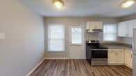 Located at 427 Lambeth Dr in Charlotte, NC, this two-story home offers a thoughtfully designed layout across two levels. The main floor welcomes you with a spacious living area finished in durable wood-look plank flooring and neutral gray walls, creating a clean, contemporary ambiance. Large windows fitted with white blinds allow natural light to fill the space, while a staircase provides seamless access to the upper level. The living area flows openly into a dining space and kitchen, where the kitchen stands out with white cabinetry featuring arched detailing, granite countertops, a stainless steel sink, a stainless steel refrigerator, and a black electric range. The kitchen also benefits from a back door with adjacent windows, providing additional natural light and outdoor access. A full bathroom on the main level includes a tub-shower combo with white tile surround. Upstairs, the bedrooms are carpeted for comfort and each features neutral gray walls and windows with blinds that bring in natural light. A second bathroom serves the upper level, appointed with a granite-top vanity, white subway tile wainscoting, and a large mirror. Throughout the home, textured ceilings and clean white trim provide a polished, move-in-ready feel.