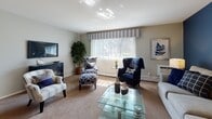 Located at 969 W Main Rd in Middletown, Rhode Island, this single-floor residence offers a thoughtfully laid-out living space with a cohesive coastal-inspired color palette throughout. The living room serves as the social heart of the home, featuring soft carpeting, a large picture window that draws in natural light and offers views of the surrounding greenery, and a striking deep-blue accent wall that adds a bold design focal point. The adjoining dining area is finished with plush carpet, a ceiling fan with integrated lighting, and ample closet storage nearby. The galley-style kitchen is equipped with warm wood cabinetry, granite-look countertops, tile flooring, and a full suite of appliances, providing a practical and efficient cooking space. The residence includes multiple carpeted bedrooms, each offering a calm, restful atmosphere with neutral wall tones, generous natural light from well-positioned windows, and ample room for furnishings. The full bathroom features tile flooring, a white vanity with stone-look countertops, and a tub-shower combination. Throughout the home, consistent finishes and a harmonious blue-and-neutral color scheme create a comfortable and inviting living environment well-suited to the Middletown, RI setting.