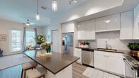 Located in the South Tampa neighborhood of Tampa, FL, this single-floor residence at 4950 W Prescott St offers a thoughtfully designed layout with modern finishes throughout. The kitchen is a standout feature, boasting high-gloss white cabinetry extending to the ceiling, dark quartz countertops, a full suite of stainless steel appliances, subway tile backsplash, and a central island with bar seating — all illuminated by sleek pendant lighting and track fixtures that create a bright, functional workspace. Wide-plank wood-style flooring flows seamlessly throughout the open-plan living and kitchen areas. The living room is inviting and well-proportioned, benefiting from natural light through large windows with sliding glass door access, complemented by neutral walls and a clean aesthetic. The bedroom is a comfortable retreat, featuring a ceiling fan, large windows dressed with sheer curtains that allow ample natural light, and continued wood-style flooring. The bathroom is finished with large-format white tile, a soaking tub with a frameless sliding glass shower enclosure, and a lighted mirror, lending a spa-like quality to the space. Throughout, the residence presents a cohesive, contemporary design with an airy, light-filled ambiance.