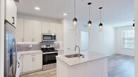 This well-appointed single-story home in Manor, TX offers a thoughtful layout with 2 bedrooms, 2 bathrooms, 2 closets, and a connecting hallway. The open-concept kitchen and living area serves as the heart of the home, showcasing a granite-topped island with an undermount sink and stylish pendant lighting overhead. The kitchen is equipped with stainless steel appliances, including a range, microwave, and refrigerator, complemented by crisp white cabinetry and a neutral tile backsplash. Light wood-style flooring flows throughout the main living areas, creating a bright and cohesive feel. A built-in mudroom nook near the entry provides convenient hooks and shelving for everyday organization. Both bedrooms are carpeted and benefit from natural light through blinds-fitted windows, with ceiling fans for added comfort. The primary bedroom is a comfortable size and connects to a well-sized walk-in closet with multi-tiered shelving and hanging rods. The bathrooms feature tiled tub-shower combinations with brushed nickel fixtures and wood-style flooring. The second closet offers equally generous storage with built-in shelving. The home's clean, modern aesthetic and practical floor plan make it a functional and attractive residence.