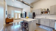 This single-floor residence combines contemporary design with practical comfort throughout its thoughtfully arranged layout. The open-concept kitchen serves as a central highlight, showcasing grey shaker-style cabinetry, white subway tile backsplash, gleaming white countertops, and a full suite of stainless steel appliances including a refrigerator, range, microwave, and dishwasher. A central kitchen island with bar seating provides additional workspace and casual dining. Soaring ceilings and an exposed industrial-style duct add architectural character to the living and kitchen areas, while polished concrete floors flow throughout, lending a clean, modern aesthetic. The living area is bathed in natural light through French doors topped with transom windows, opening to an outdoor space. Two well-appointed bedrooms offer comfortable retreats, each with ample natural light from large windows. The primary bathroom features dual vanity sinks with grey cabinetry and a tub-shower combination, while the secondary bathroom offers a similarly clean, neutral design with a tub-shower. A dedicated laundry room with a full-size washer and dryer adds everyday convenience, completing this well-designed residence.