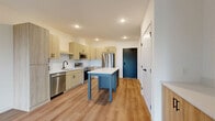 Located at 11816 Wayzata Blvd in Minnetonka, MN, this modern one-bedroom, one-bathroom unit offers a well-designed single-floor layout with contemporary finishes throughout. The open-concept kitchen and living area serves as the heart of the space, featuring light wood cabinetry, a white subway tile backsplash, stainless steel appliances including a refrigerator, dishwasher, and range, and a central kitchen island with a crisp white countertop. Recessed lighting and durable wood-style flooring run throughout the main living area, which is bathed in natural light from large floor-to-ceiling windows and a sliding glass door that opens to a private balcony with views of surrounding greenery. The bedroom is a comfortable, carpeted retreat equipped with a ceiling fan, a large black-framed window overlooking lush outdoor scenery, and ample closet access. The bathroom features a warm wood vanity with black hardware, a white countertop, a tiled walk-in shower, and wood-style flooring that ties cohesively to the rest of the unit. Additional spaces include a laundry room, utility room, and multiple closets, providing generous storage throughout. The overall aesthetic is clean, modern, and bright.