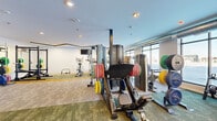 Located at 5605 38th St S in Fargo, North Dakota, this fitness studio offers a thoughtfully designed single-floor exercise space that accommodates a wide variety of workout needs. The room features a modern aesthetic with a multi-toned carpet layout in shades of gold, green, and grey that visually zones the space and adds a contemporary feel.

Architecturally, the studio stands out with its distinctive geometric linear LED lighting installed across the ceiling, providing both functional illumination and a stylish design element. Large windows along one wall flood the space with natural light and offer open views of the surrounding area, contributing to an energizing workout atmosphere.

The equipment selection is extensive and well-organized. Cardio offerings include multiple Spirit treadmills and stationary bikes, complemented by wall-mounted TVs for entertainment. The strength training area is equally robust, featuring a power rack, a leg press machine, a multi-station cable machine, dumbbells, kettlebells, barbells with color-coded weight plates, and adjustable benches. Medicine balls and additional free weights round out the offerings. A full-length mirror along one wall enhances the sense of space and supports proper form during workouts. The studio is accessible via clearly marked entry and exit doors, making it a practical and well-appointed facility for a comprehensive fitness regimen.