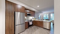 This single-floor residence in Oakland, CA offers a thoughtfully designed interior with modern finishes and a cohesive aesthetic throughout. The kitchen is a standout feature, equipped with a full suite of stainless steel appliances including a gas range, built-in microwave, French door refrigerator, and dishwasher. Rich walnut-toned cabinetry extends to the ceiling, complemented by a white subway tile backsplash, light quartz countertops, and wood-look plank flooring that flows seamlessly through the space.

The living area is bright and welcoming, with large windows fitted with horizontal blinds allowing generous natural light and outdoor views. A dedicated dining nook features a round dark-topped table beneath a statement pendant light, creating an intimate setting. The bedroom is spacious and serene, complete with a ceiling fan, large windows, and access to a well-sized walk-in closet outfitted with wire shelving and hanging rods. The bathroom maintains the same refined palette, with walnut cabinetry, white quartz countertops, light plank flooring, and a large mirror. Neutral tones and clean lines unify the entire residence.