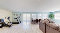 Located at 2520 Suffolk Ave in High Point, NC, this single-floor community space offers a practical and comfortable layout designed to serve residents with ease. The interior is finished throughout with large white ceramic floor tiles that reflect natural light and contribute to a clean, open feel.

The combined living and dining area forms the heart of the space, painted in a soft aqua-blue tone that lends a calm, airy ambiance. The living area is anchored by a generously sized sectional sofa and features recessed lighting, a wall-mounted television, and a sliding glass door with vertical blinds that opens to an outdoor deck. Multiple windows along the dining side flood the space with natural light, framing views of the surrounding exterior. A large dining table with ample seating makes this area well-suited for group gatherings.

Adjacent to the main living space, a kitchen counter area provides additional utility, while a separate zone accommodates fitness equipment, adding a practical wellness component to the layout.

The dedicated laundry room is a standout functional feature, housing a full row of commercial-grade front-loading washers and dryers along one wall, complemented by a folding table, seating, and a light yellow color palette. A glass-paneled exterior door provides direct outdoor access, enhancing ventilation and convenience. This well-appointed space serves as a comprehensive community amenity.