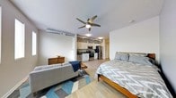 This thoughtfully designed studio offers an open-concept floor plan that effortlessly combines the living, sleeping, and kitchen zones into one cohesive, functional space. Light-toned hardwood-style flooring extends throughout, lending warmth and visual continuity across every area. A ceiling fan with an integrated light fixture anchors the main living space, promoting airflow and comfort year-round.

The kitchen is outfitted with white shaker-style cabinetry, stainless steel appliances — including a refrigerator, range, and microwave — and a clean, modern aesthetic. Exposed ductwork along the upper walls adds an industrial character that complements the contemporary design.

The living area accommodates a comfortable sofa and a wooden side table, anchored by a geometric-patterned area rug in blue and gray tones that defines the space. The sleeping area features a platform bed with a warm wood frame, positioned to take full advantage of the open layout.

Neutral white walls and consistent, recessed lighting keep the interior feeling bright and airy. The single-floor layout maximizes accessibility and ease of movement throughout. Overall, the space strikes a balance between modern urban style and practical everyday living, making it a functional and inviting environment.