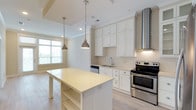 This single-floor residence is designed with a clean, contemporary aesthetic highlighted by a bright, neutral color palette throughout. The kitchen serves as a standout feature, showcasing floor-to-ceiling white shaker cabinetry, light quartz countertops, and a decorative arabesque tile backsplash. Stainless steel appliances, including a French door refrigerator, electric range, and dishwasher, are complemented by a sleek stainless steel range hood. A central island with open shelving provides additional prep and storage space, while two industrial-style pendant lights add a stylish focal point. Light hardwood flooring runs throughout the kitchen and main living areas.

A separate living area features large windows and a glass door that invite abundant natural light and offer views of the surrounding exterior. The bedrooms are finished with plush carpet and ceiling fans, creating a comfortable retreat. One bedroom benefits from an adjacent bathroom featuring a dual-sink vanity with white cabinetry and large-format tile flooring. A walk-in closet with multi-tier wire shelving provides generous storage. Crown molding and recessed lighting are consistent throughout, contributing to a polished and cohesive interior.