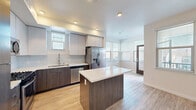 Located at 1185 Vintage Ln in Morgan Hill, California, this single-floor residence showcases a thoughtfully designed contemporary interior with consistent finishes throughout. The open-concept kitchen is a standout feature, equipped with stainless steel appliances including a gas range, microwave, refrigerator with ice and water dispenser, and dishwasher. Two-toned cabinetry — combining dark wood lower cabinets with light upper cabinets — pairs elegantly with a white quartz countertop island that provides additional workspace and casual seating. A subtle mosaic tile backsplash adds texture to the kitchen walls, while recessed lighting illuminates the space efficiently. Light wood-tone flooring flows seamlessly throughout the home, contributing to a bright, cohesive aesthetic. Large windows fitted with horizontal blinds invite abundant natural light into the living area, which opens directly from the kitchen for an airy, connected feel. The bedroom offers a walk-in closet and multiple windows that fill the room with daylight. The bathroom features a full tub-shower combination with sliding glass doors and clean, white tile surround. The home's overall design is clean, modern, and move-in ready.