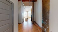 Located at 601 S Fifth St in Easley, South Carolina, this single-floor loft-style unit is a striking adaptive reuse of a historic industrial building. Original hardwood floors run throughout, complemented by exposed brick walls bearing layers of aged paint that speak to the building's rich history. Soaring ceilings with original timber beams and heavy-duty steel columns anchor the open, airy layout, while exposed ductwork adds to the authentic industrial aesthetic.

Large multi-pane windows flood the living areas with abundant natural light, casting dramatic geometric shadows across the warm wood floors. A ceiling fan with ample blade span serves the spacious main living area. The kitchen features gray shaker-style cabinetry, marble-look countertops, stainless steel appliances including a gas range and side-by-side refrigerator, and a central island — all framed by an original structural column.

The unit includes generously sized rooms with soaring wall heights, providing a versatile and open feel. Two bathrooms are present: one with a walk-in shower, and another with ADA-accessible features including grab bars and a marble-top vanity. Gray-paneled interior doors and coordinated trim offer a polished contrast to the raw, historic materials throughout, creating a refined yet industrial ambiance.