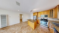 Located at 760 Embarcadero del Norte in Goleta, CA, this one-bedroom, one-bathroom unit offers a well-designed single-floor layout with a cohesive, functional living space. Warm-toned tile flooring runs throughout, providing a unified aesthetic from room to room.

The kitchen is a standout feature, equipped with stainless steel appliances including a refrigerator, gas range, built-in microwave, and dishwasher. Warm wood cabinetry with glass-front upper panels complements the granite countertops and tile backsplash. A central island with additional granite surface space adds both functionality and visual interest. Recessed lighting and a track light fixture brighten the space effectively.

The bedroom is a comfortable size, enhanced by natural light streaming through a large window fitted with vertical blinds. A dedicated closet provides ample storage.

The bathroom features tile flooring, a sliding glass-door shower enclosure, and a dark wood wall cabinet for added storage.

A private balcony accessible from the unit overlooks a palm-lined street, offering pleasant outdoor views characteristic of the Southern California coastal setting. The ceiling fan with integrated lighting in the main living area adds a practical and decorative touch. Overall, the unit presents a clean, well-maintained interior in a vibrant Goleta neighborhood.