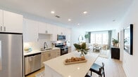 Located at 9111 Paragon Dr in Charlotte, NC, this well-appointed 2-bedroom, 2-bathroom residence offers a thoughtfully designed single-level layout with a clean, modern aesthetic throughout. Light wood flooring flows seamlessly across every room, complemented by crisp white walls and recessed lighting that create a bright, airy ambiance.

The open-concept kitchen and living area serves as the heart of the home. The kitchen features white upper cabinetry, warm wood lower cabinets, stainless steel appliances including a side-by-side refrigerator and dishwasher, a subway tile backsplash, and a built-in bench nook. The adjoining living room offers generous natural light through large windows with views of the community grounds.

The primary bedroom is a calm retreat, accented by warm sconce lighting and easy access to a spacious en-suite bathroom. This bathroom includes a double-sink vanity with black hardware, light wood flooring, and a glass-enclosed walk-in shower. The second bedroom features a ceiling fan, floor-to-ceiling windows, and direct balcony access, where views open onto manicured green lawns and the surrounding community. A dedicated walk-in closet with wire shelving provides practical storage. The second full bathroom includes a soaking tub with shower, white cabinetry, and black fixtures throughout.