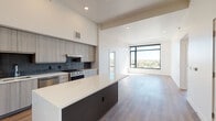 This contemporary single-floor residence showcases a thoughtfully designed open-concept layout with clean lines and modern finishes throughout. The kitchen is a standout feature, boasting soaring ceilings, sleek two-tone cabinetry, a bold tile backsplash, stainless steel appliances, and a central island with a crisp white countertop — ideal for both cooking and entertaining. Wide-plank hardwood-style flooring flows seamlessly from the kitchen into the expansive living area, which is bathed in natural light from large floor-to-ceiling windows offering sweeping city and treetop views.

The bedrooms are generously proportioned, carpeted for comfort, and feature ceiling fans and large windows that frame bright outdoor vistas. The primary bathroom is well-appointed with a dual-sink vanity, dark cabinetry, subway-tiled tub-shower, and a walk-in closet with built-in shelving. A second bathroom mirrors the modern aesthetic with similar tile work and a clean, minimalist vanity. A dedicated laundry room with a full-size washer and dryer adds everyday convenience. The unit's neutral palette, recessed lighting, and consistent high-quality finishes create a cohesive, move-in-ready living environment.