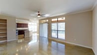 Located at 105 N Austin Ave in Georgetown, Texas, this single-story space offers a thoughtfully designed open-concept layout that seamlessly connects the living and kitchen areas. The interior is anchored by striking polished concrete floors that reflect light throughout, lending a clean, modern aesthetic to the space.

Large windows with transom accents line the walls, inviting an abundance of natural light and offering views of the surrounding greenery. Vertical blinds provide flexible light and privacy control. A ceiling fan with a classic fixture adds both function and character to the main living area.

The kitchen is well-appointed with rich dark wood cabinetry, a kitchen island with a built-in sink, pendant lighting overhead, and its own set of large windows that keep the space bright and airy. Recessed lighting in the kitchen complements the pendant fixtures, ensuring thorough illumination throughout.

Crown molding details along the ceiling add a polished architectural touch, while the neutral warm-toned walls create a versatile backdrop suitable for a variety of uses. The open flow between the kitchen and main living area makes this space ideal for both everyday function and entertaining. Overall, the space combines practical design with inviting, light-filled interiors in a desirable Georgetown location.