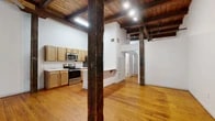 Located at 301 Crockett St in the heart of downtown Shreveport, Louisiana, this single-floor unit masterfully blends historic industrial character with modern updates. Original hardwood floors stretch throughout the open layout, complemented by soaring ceilings defined by richly toned exposed wooden beams and wood plank decking — a hallmark of the building's storied past. Massive original timber support columns anchor the main living area, adding bold architectural drama to the space.

The open-concept kitchen and living room form the heart of the unit. The kitchen is well-appointed with warm maple cabinetry, stainless steel appliances including a range, microwave, and refrigerator, and striking marble-look countertops that extend to a peninsula with an undermount sink — ideal for dining or casual seating. The living area flows naturally from the kitchen, offering an airy, loft-like atmosphere enhanced by track lighting.

A dedicated living room provides additional space for relaxing or entertaining, while a separate room features an exposed brick accent wall and a window that brings in natural light, offering a warm, textured backdrop. The bathroom includes a full tub-shower combination. In-unit laundry is provided via a stacked washer and dryer. The unit also features ceiling fans for added comfort throughout.