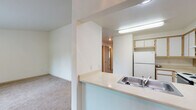 This single-floor residence features a thoughtfully arranged open-concept design that connects the kitchen, dining, and living areas into one cohesive space. The kitchen is well-equipped with white cabinetry trimmed in light wood, a full suite of appliances including a refrigerator, electric range, and dishwasher, and generous counter space along a U-shaped layout. A peninsula with a stainless steel sink extends into the adjoining area, creating a natural divide between the kitchen and the living space while maintaining an open, connected feel. The living area features durable hardwood-style flooring, a ceiling fan, a baseboard heater, and sliding glass doors that invite natural light and provide outdoor access. Adjacent carpeted areas offer comfortable, quiet spaces ideal for bedrooms, each receiving natural light through windows overlooking lush greenery. The bathroom includes wood-style flooring, a vanity with built-in storage, and a sizable closet nearby. Throughout the unit, neutral white walls and light-toned finishes create a clean, bright ambiance. The 3D floor plan overview confirms the efficient, well-proportioned layout of the entire space.